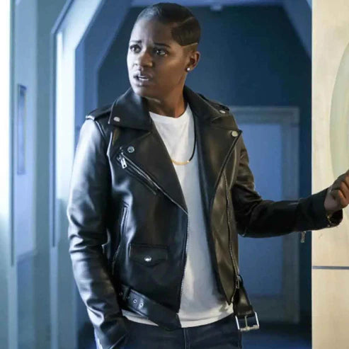 A person wearing a black biker leather jacket with a white shirt underneath, standing in a dimly lit indoor setting.